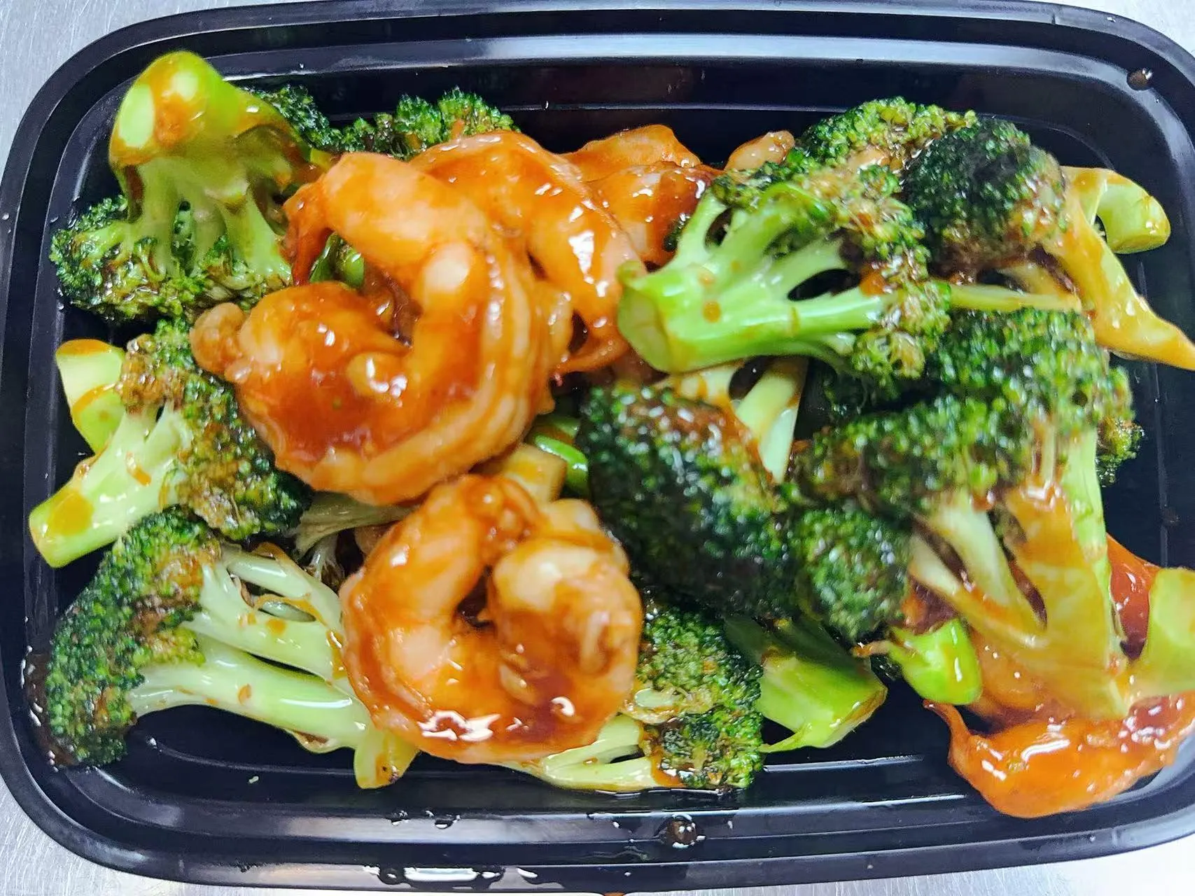 Glazed shrimp stir-fried with fresh broccoli in black plastic takeout tray at Silk Road Bistro, a Chinese Restaurant in Martiborough